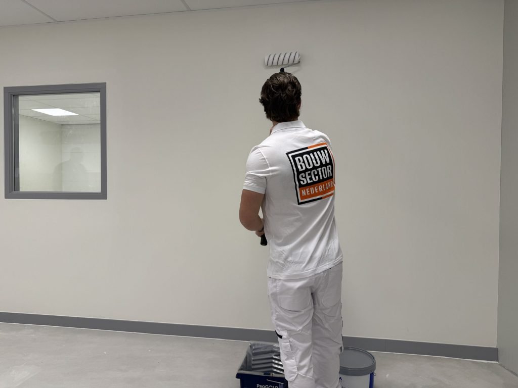 Schilder op de rug gezien zet met de roller een witte laag bovenaan de muur