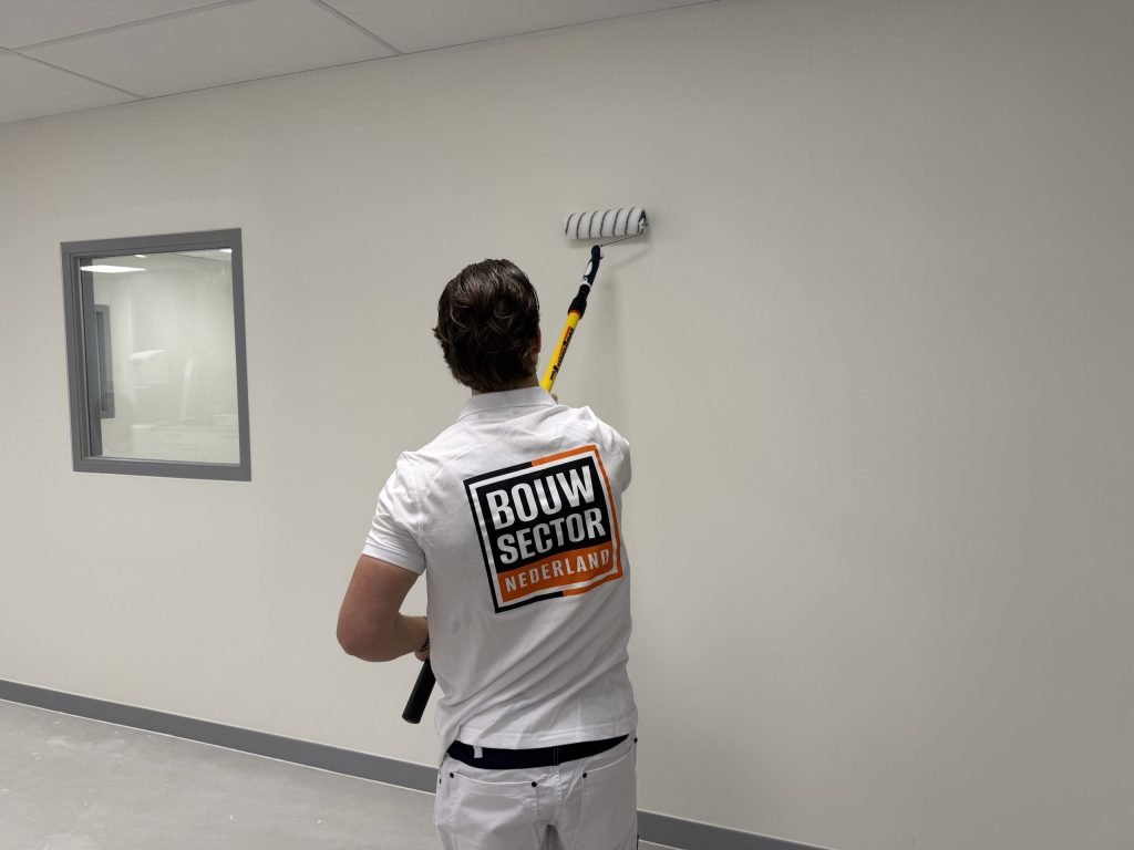 Schilder van Bouwsector Nederland rolt een lichte muur in een lege kamer met een raam