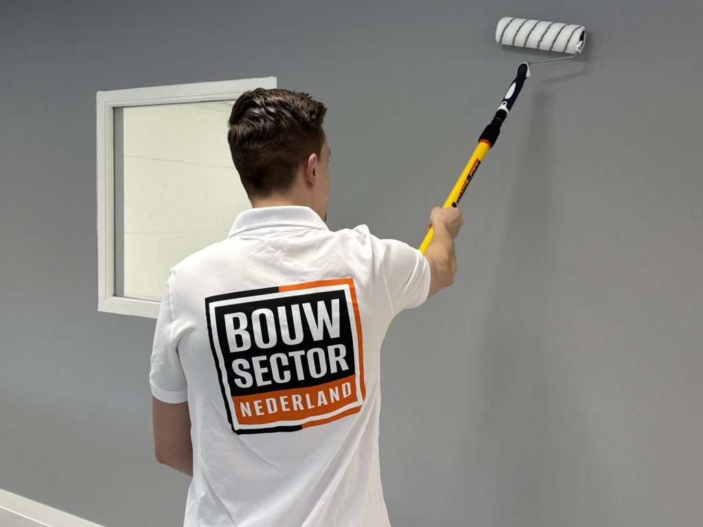 Schilder in wit shirt van Bouwsector Nederland verft een grijze muur naast een raam met witte omlijsting