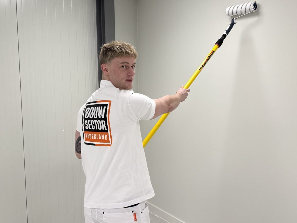 Schilder kijkt over zijn schouder terwijl hij een lichte muur met de roller saust