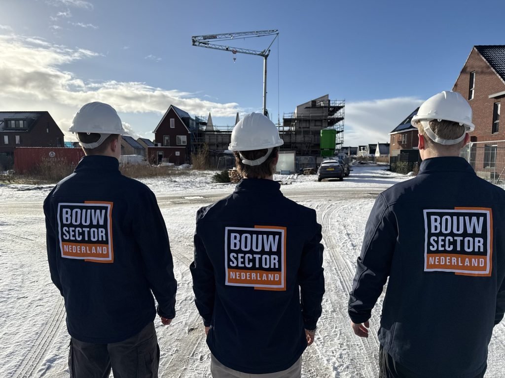 Drie vakmensen van Bouwsector Nederland met witte helm en logo op de rug bij nieuwbouw in aanbouw met een bouwkraan